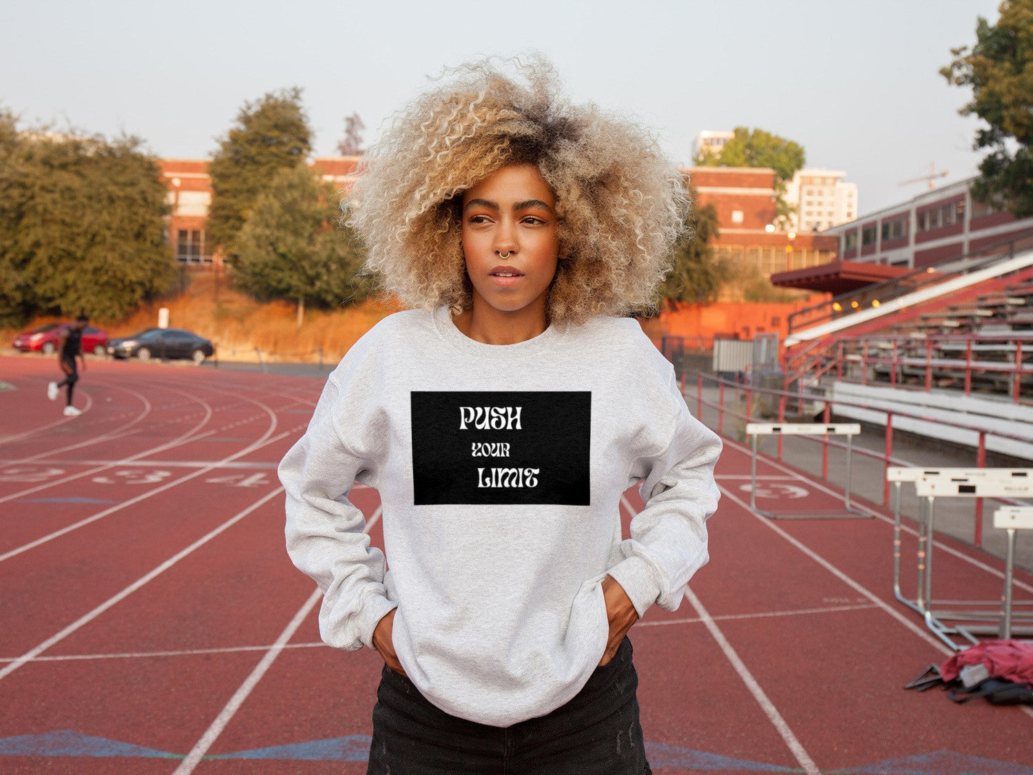 Young woman on a sports field wearing a sweatshirt with the slogan “Push your limits”.